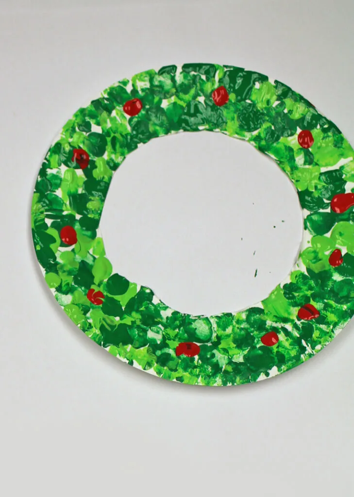 Painted paper plate shaped wreath with red dots for holly.